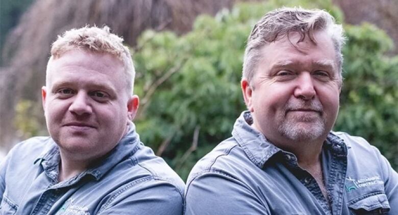 Two white men with arms folded look into the camera.