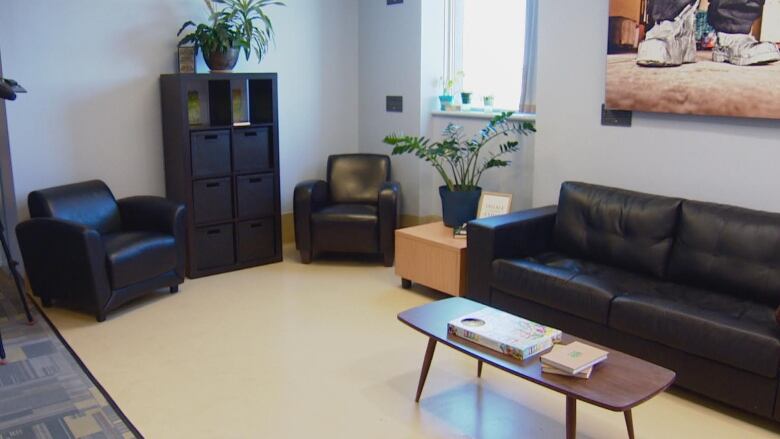 A room with a black couch and two black chairs. A coffee table has books and a board game on it. 