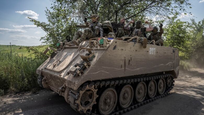 A group of men in camouflage uniforms ride on top of a large metal vehicle. 