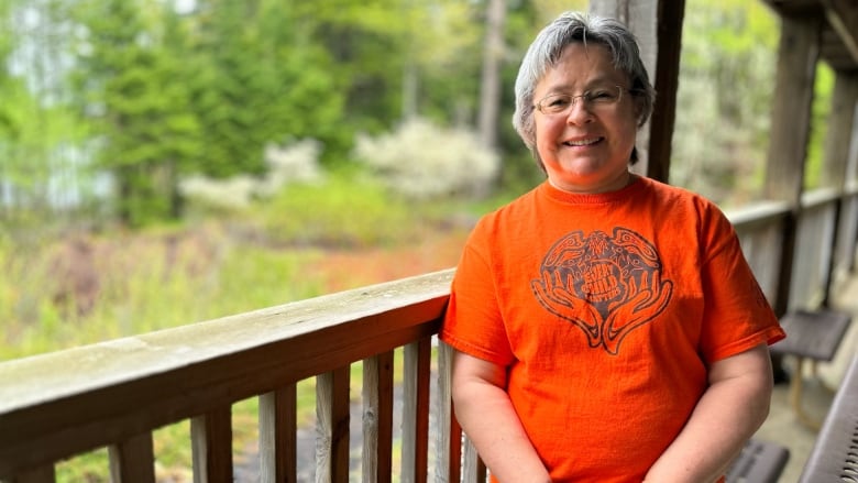 A woman wearing an orange shirt that says 'every child matters' stands on a wooden porch.