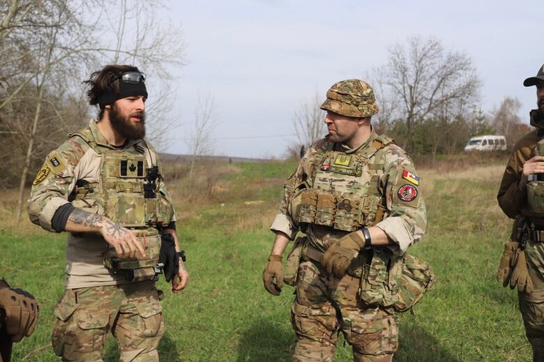 Three people wearing military uniforms stand in a field.