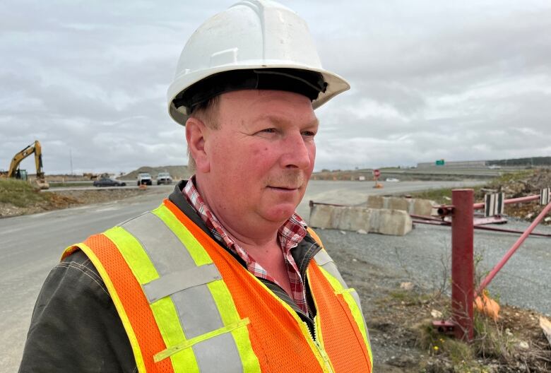 A man wearing construction gear standing on a dirt road.