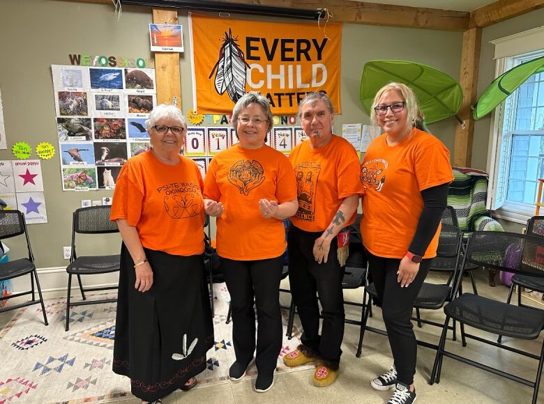 Three women and a man wearing orange shirts stand in a line.