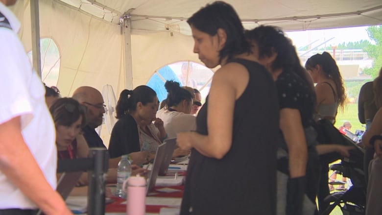 A group of people are seen lining up to speak to a row of workers along a table.