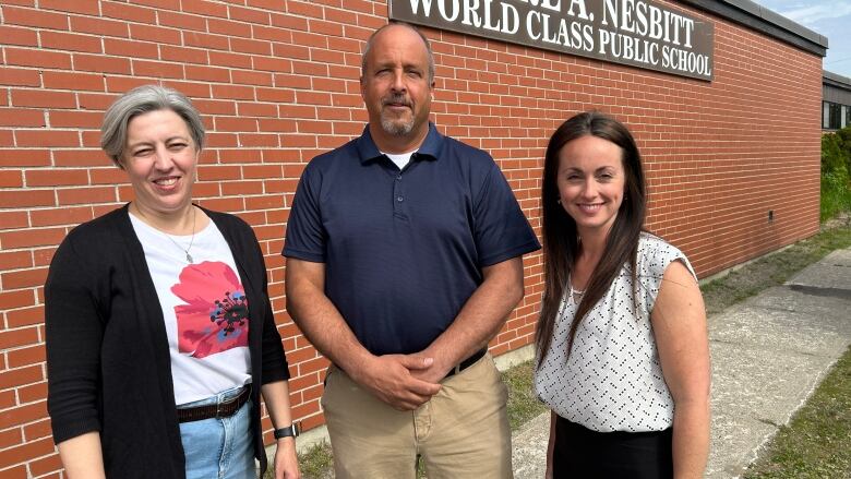 Two women and a man standing outside a brick school.