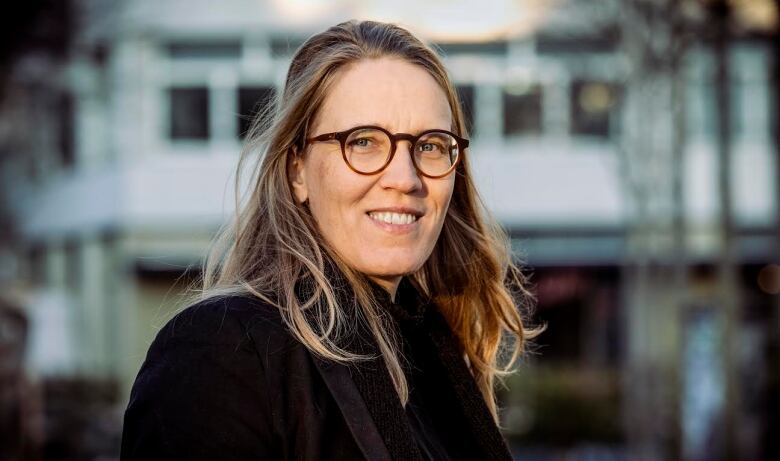 A woman with glasses smiles in this headshot. 