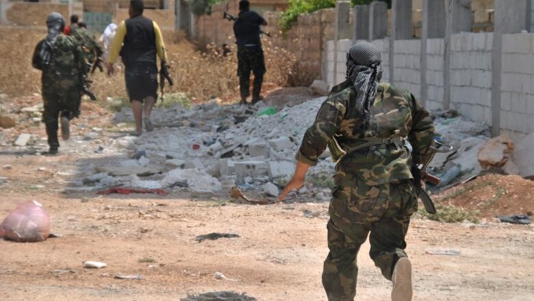 In this picture taken on Saturday, June 23, 2012, Syrian rebels run during clashes with Syrian government forces, at Saraqeb town, in the northern province of Idlib, Syria. Investigators say they have concluded that Syrian government troops could be behind the killing of more than 100 civilians in the village of Houla last month. The findings, which were presented to the U.N.'s top human rights body, could lay some of the groundwork for prosecuting alleged crimes against humanity or war crimes in Syria.