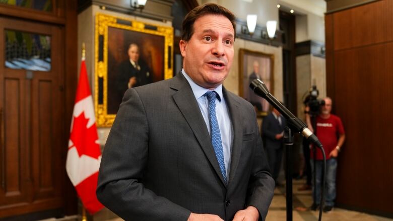 A man in a suit standing at a microphone in a foyer.