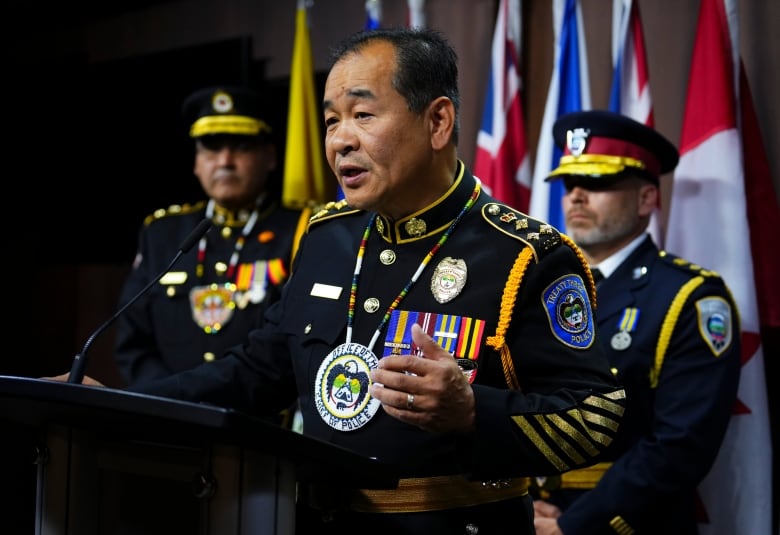 A police officer standing at a podium with two other officers in the background.