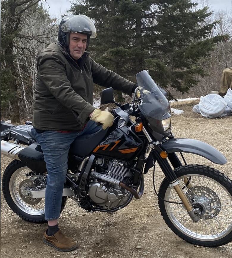 A man sits on a dirt bike, wearing a helmet and looking at the camera.