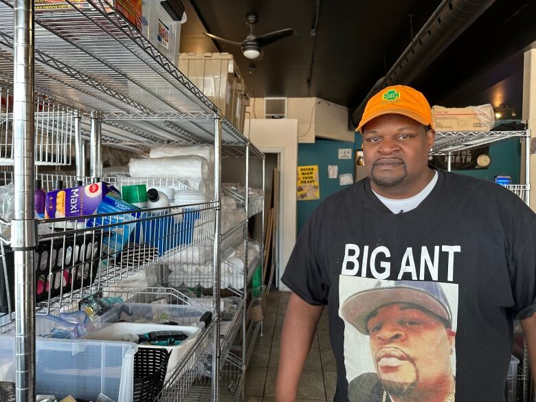 A man stands in a room beside metal racks with supplies like deodorant on them.