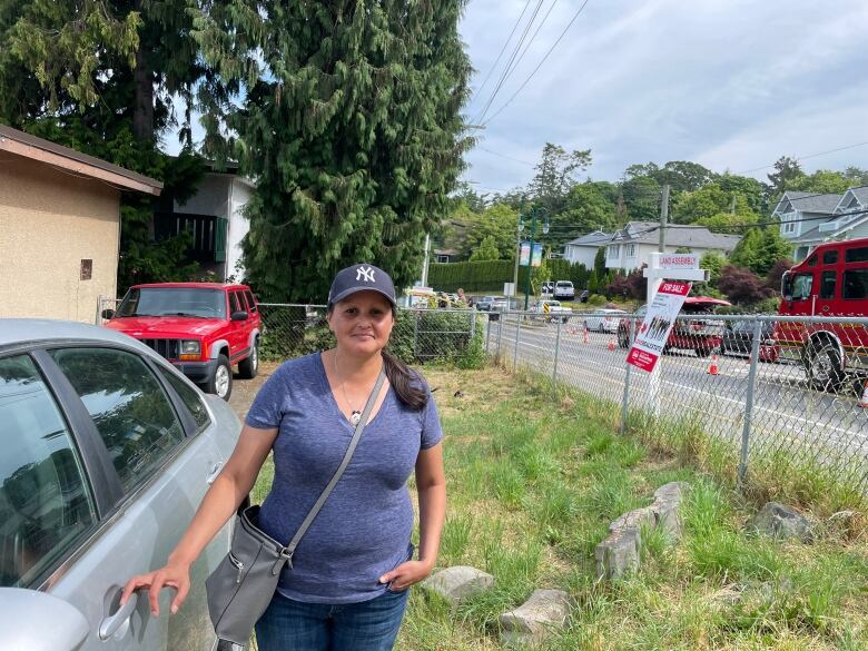 A woman in a baseball hat stands next to a road with emergency vehicles.