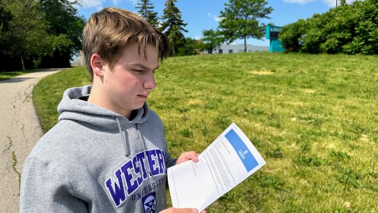 Teenage boy wearing Western University hoodie looks at a rejection letter from Queen's University 