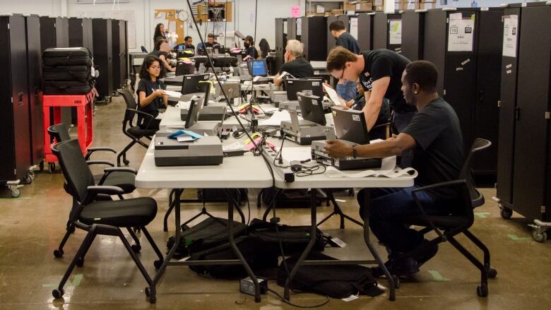 People are seen running a voting station indoors.