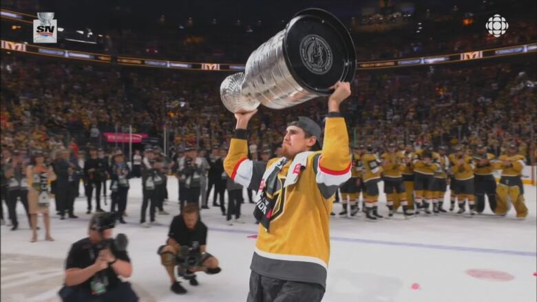 Hockey player lifts Stanley Cup over his head.