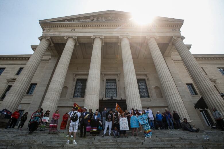 A few dozen people stand on the steps of the Manitoba Legislature.