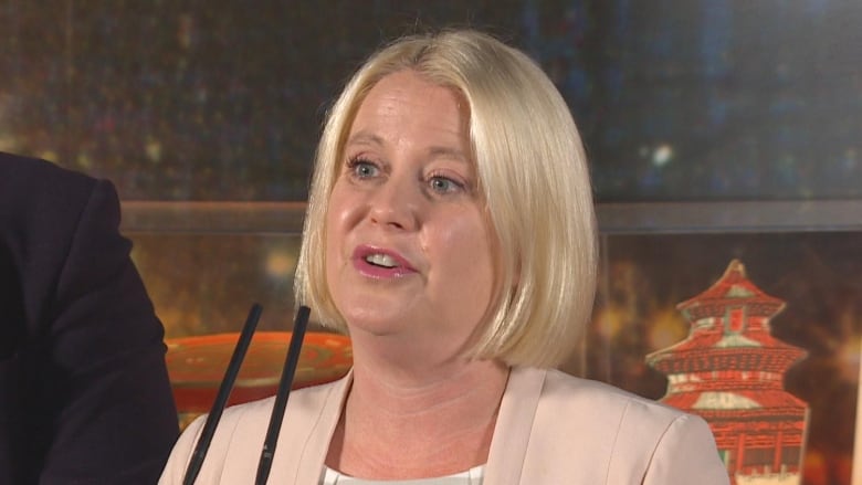 A white woman with short blonde hair speaks at a podium.