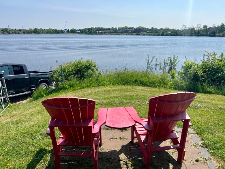 Two empty, red beach chairs are seen overlooking a lake