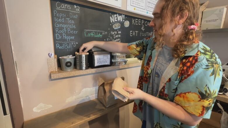 An employee in a shirt with pineapples on it reaches for cutlery while holding a napkin.