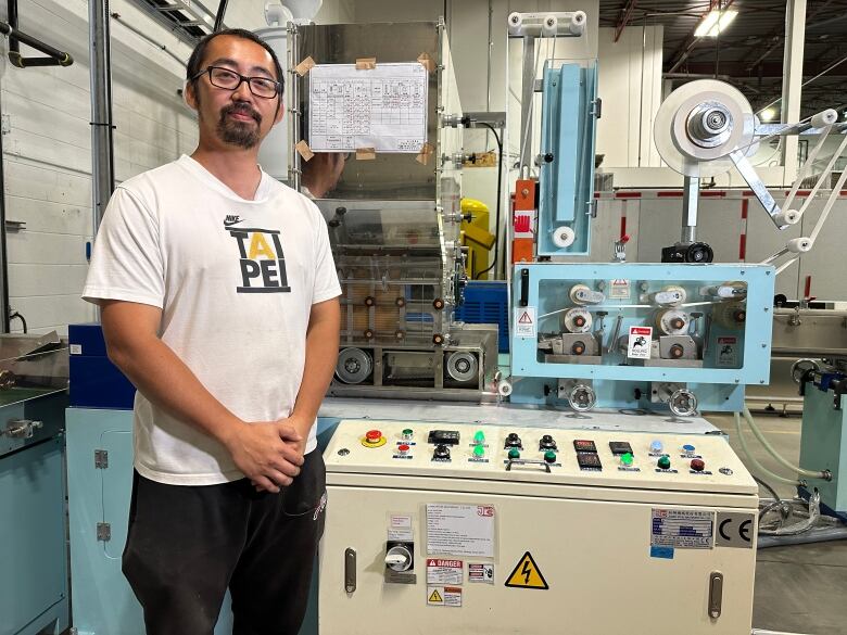 A man stands in front of a machine that wraps straws in paper.