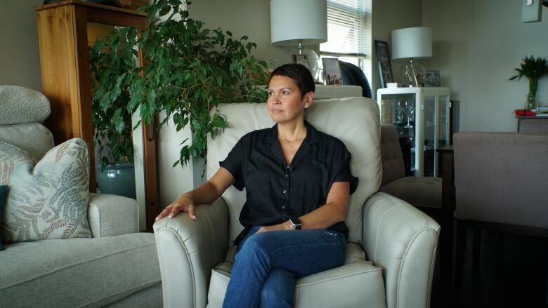 A woman is pictured sitting on a white leather chair in a home. 