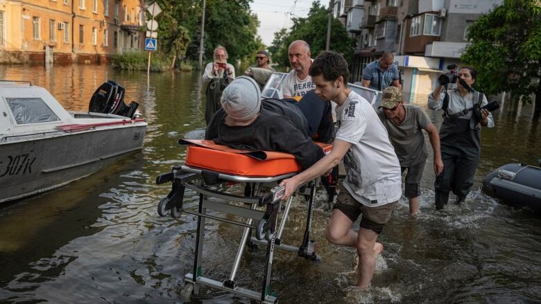 Volunteers haul a woman on a stretcher through a flooded street.