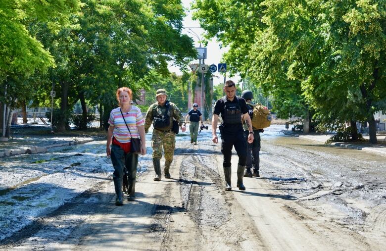 People walk through muddy streets in bright sunshine.