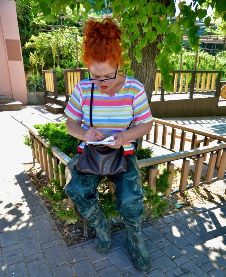 A woman wearing muddy boots takes notes.