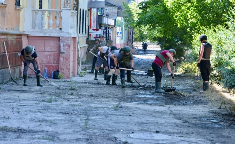 People in body armour shovel mud off a sidewalk.