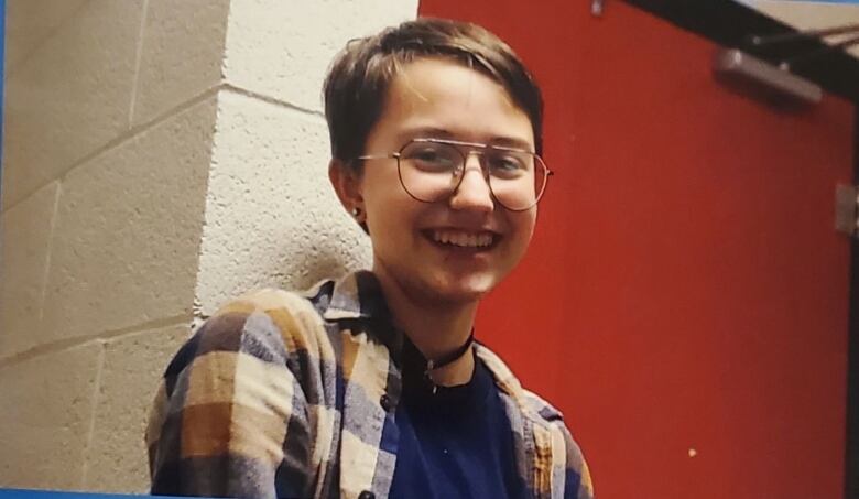 A boy with short hair and glasses wearing a flannel shirt. 