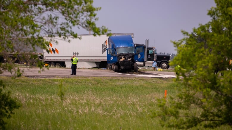 A semi trailer with a burned front end is pictured in the middle of a highway.