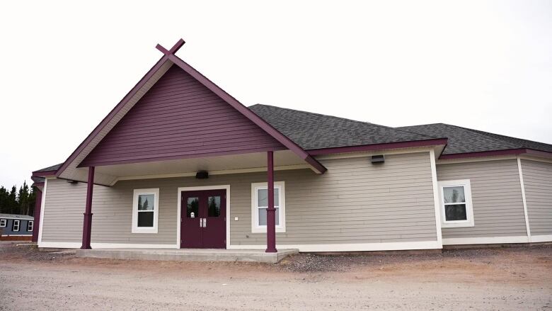 A tall buildling has a black roof, beige siding and a purple triangle point. 