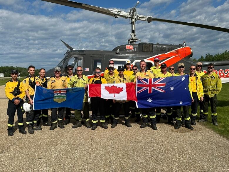 Firefighters in yellow shirts hold up Alberta, Canada and Australian flags.