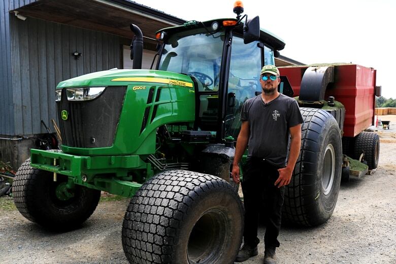 A man stands by a large green tractor.