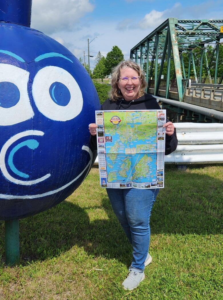 A woman holds a map in front of a blueberry statue