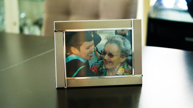 A framed photograph on a table shows a close-up of a young woman embracing an elderly woman. 