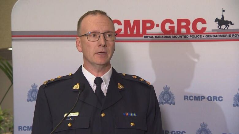 A man in a police uniform stands at a podium in front of an RCMP banner.