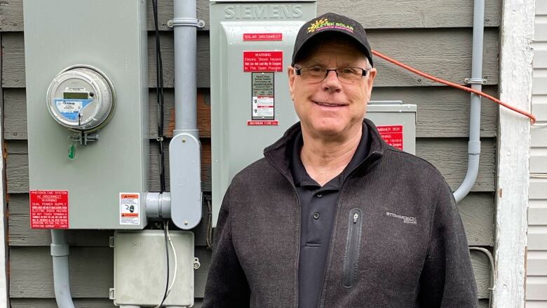 A man with glasses stands in front of a power hookup outside of a home.