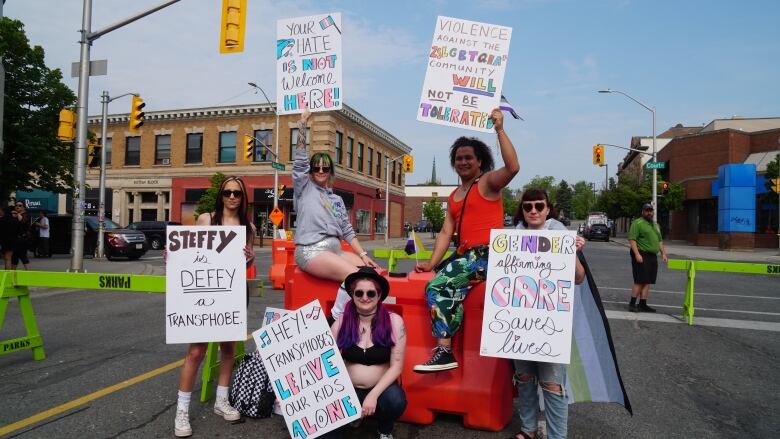 Five individuals hold different signs expressing support for the transgender and LGBTQ communities.