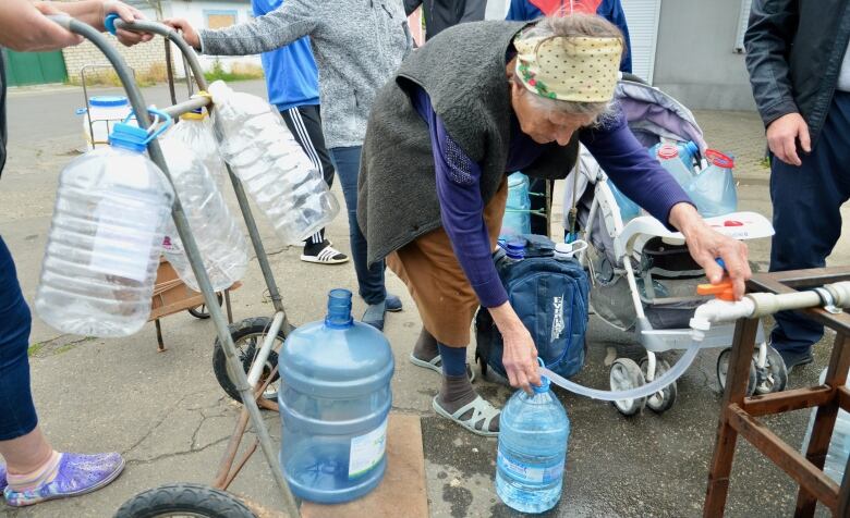 Unidentified elderly woman fills a water jug at a mobile relief station in Mykolaiv.