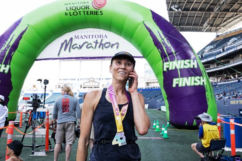 A woman, after finishing a marathon, holds the phone and smiles while speaking with her husband.