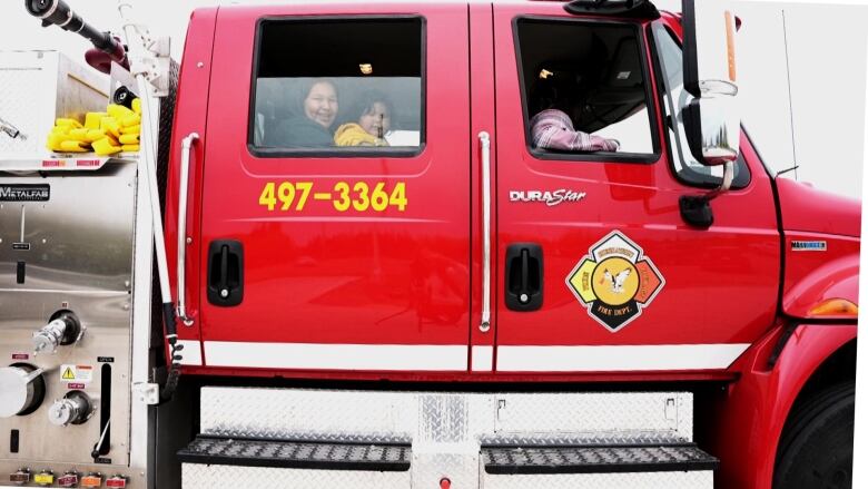 A red fire trruck sits on a driveway with kids sitting in the seats. 