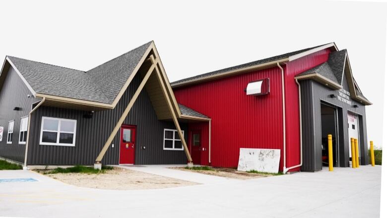 A red garage is attacehd to a dark blue building. 