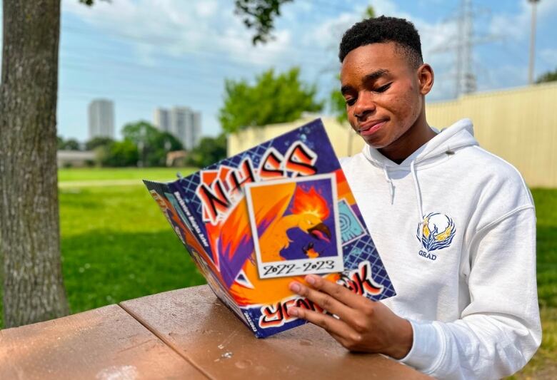 Student sitting outdoors at a picnic table looks through his high school yearbook. 