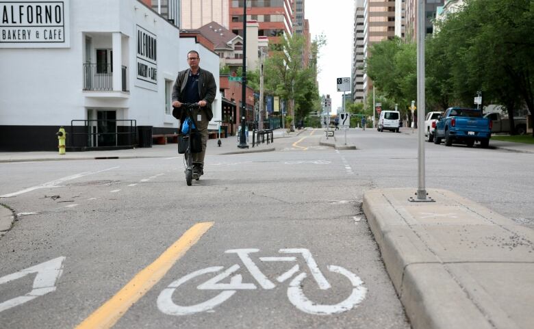 A man rides a scooter in a separated bike lane in downtown Calgary.