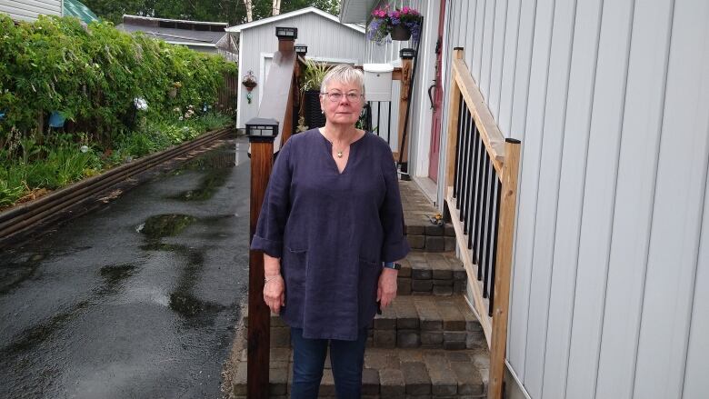 An older woman standing outside her home.