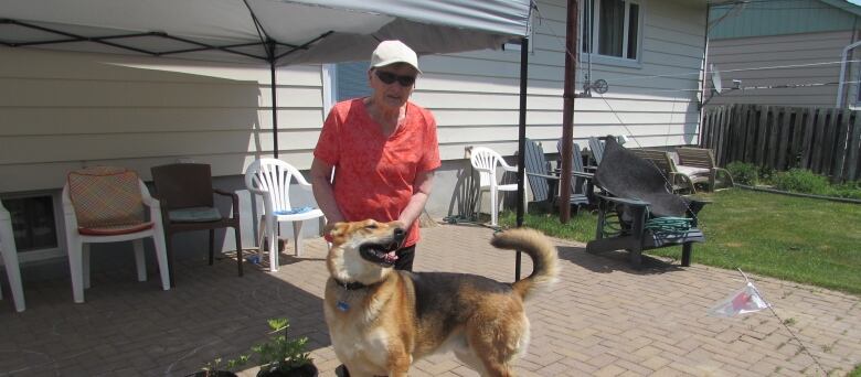 A woman standing outside ahome with a dog.