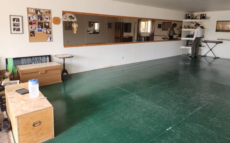 A man dressed in white wearing a cowboy hat stands in the corner of a large room with mirrors and a green floor.