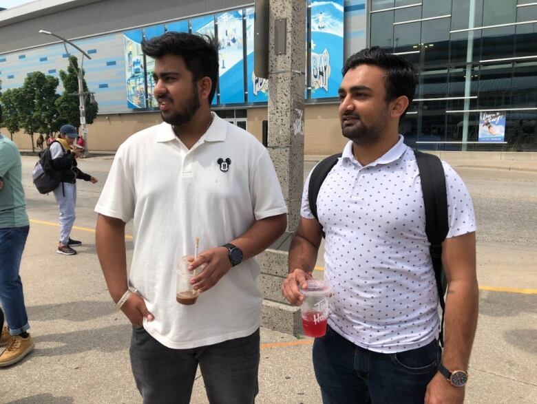 Two men wearing white polo t-shirts standing beside each other looking to the left at a bus stop