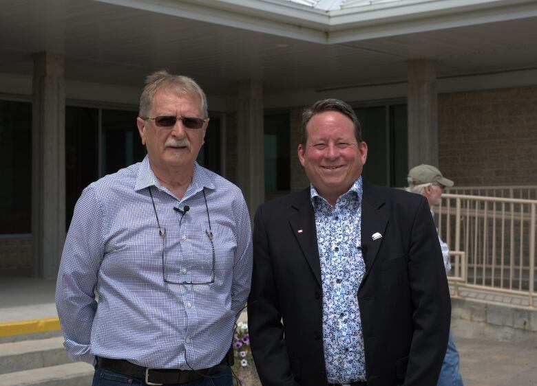 Two municipal councillors stand shoulder to shoulder outside a council building.